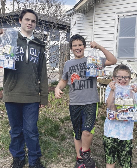Kassi’s three sons share smiles while holding Food 4 Kids packets of nutritious food.